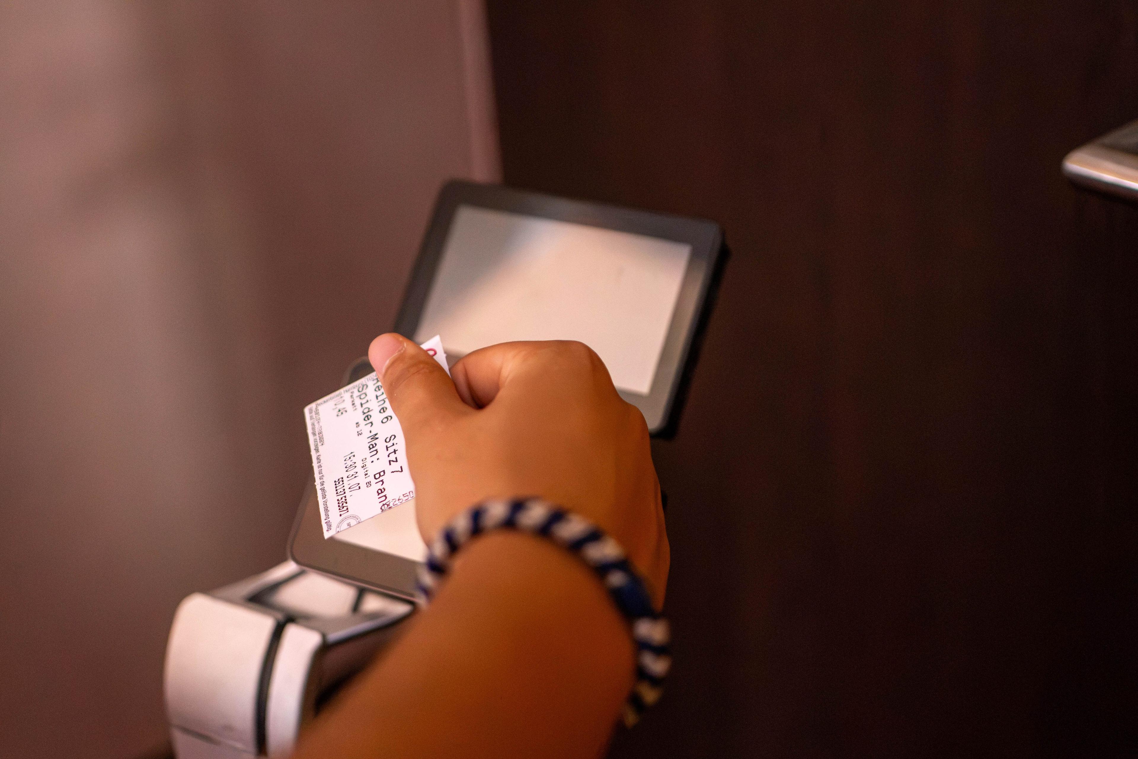 A person's hand with a striped bracelet placing a ticket into a digital reader.