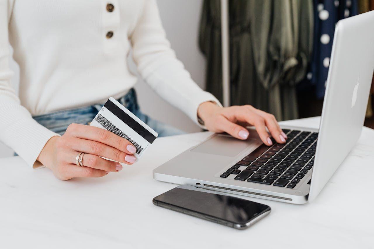 Person uses a credit card while typing on a laptop for an online transaction.